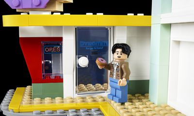 Το ειδώλιο Lego του Jungkook κρατά ντόνατ Lego έξω από ένα κατάστημα με ντόνατ Lego.