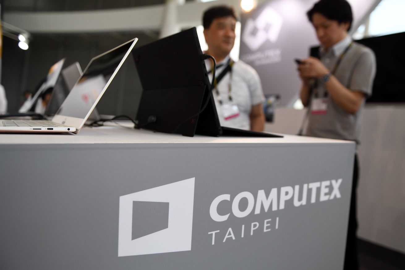 Δύο επισκέπτες στέκονται πίσω από ένα γραφείο με το λογότυπο Computex κατά τη διάρκεια του Computex 2018 στο εκθεσιακό κέντρο Nangang στην Ταϊπέι.