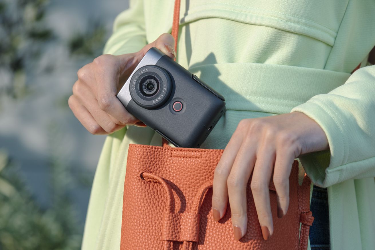 Ένα άτομο που αφαιρεί την κάμερα vlogging Canon PowerShot V10 από μια πορτοκαλί τσάντα.